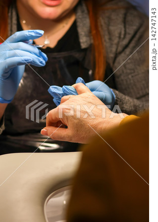 Nail technician wearing blue gloves performing a manicure procedure on a client's hand in a salon. Beauty, care, and hygiene concept Nail technician wearing blue gloves performing a manicure procedure on a client's hand in a salon. Beauty, care, and hygiene concept 142747143