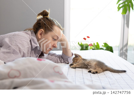 Woman watching a curious kitten on a bed at home 142747756