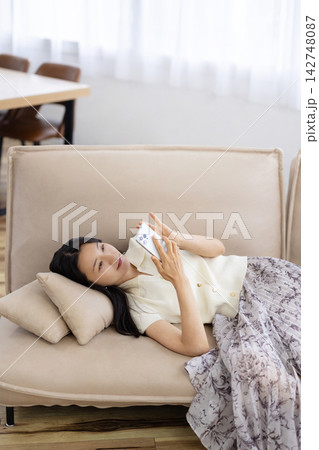 ソファに寝転んでスマートフォンを操作する若い日本人女性 ソファに寝転んでスマートフォンを操作する若い日本人女性 142748087