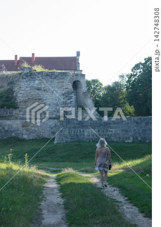 Woman Walking Along Dirt Path Toward Ancient Stone Castle Wall on Sunny Day Woman Walking Along Dirt Path Toward Ancient Stone Castle Wall on Sunny Day 142748308