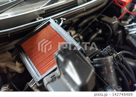 Clean orange engine air filter exposed inside vehicle engine bay during inspection maintenance replacement automotive servicing Clean orange engine air filter exposed inside vehicle engine bay during inspection maintenance replacement automotive servicing 142748489