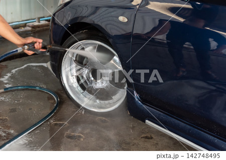 Worker pressure washing car wheel tire powerful water spray during professional vehicle cleaning detailing maintenance service Worker pressure washing car wheel tire powerful water spray during professional vehicle cleaning detailing maintenance service 142748495