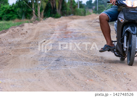 Motorcycle rider traveling an uneven rural dirt road gravel dust representing countryside transportation road conditions mobility infrastructure Motorcycle rider traveling an uneven rural dirt road gravel dust representing countryside transportation road conditions mobility infrastructure 142748526