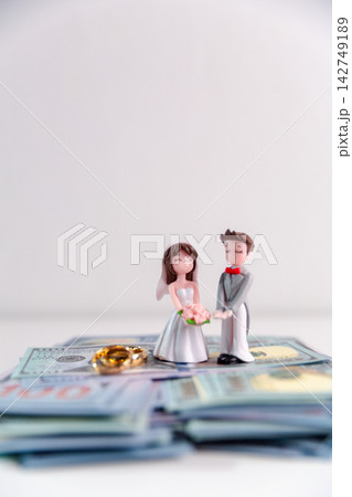 Bride and groom figurines standing on stacks of banknotes with gold wedding rings, representing wedding budgeting, marriage finance, savings, and financial planning for married life. Bride and groom figurines standing on stacks of banknotes with gold wedding rings, representing wedding budgeting, marriage finance, savings, and financial planning for married life. 142749189