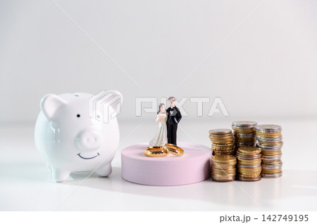 Piggy bank, wedding couple, gold rings and stacked coins on a clean white background, representing wedding savings, marriage budget, couple finances and financial preparation. 142749195