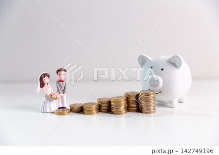 Bride and groom figurines beside a white piggy bank and growing stacks of coins, symbolizing saving for marriage, wedding budgeting, and financial planning for a secure future. 142749196