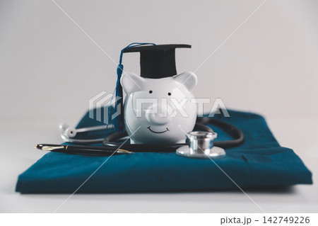 Piggy bank wearing a graduation cap with a stethoscope symbolizes medical education, career investment, student savings, healthcare training, tuition costs and financial planning. 142749226