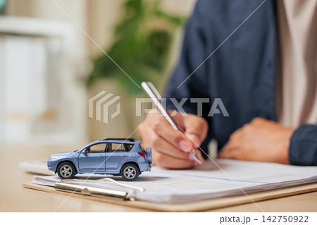 A man writes his signature on a car finance or lease agreement. Great for vehicle buying, renting, or dealership deals emphasizing auto loans 142750922