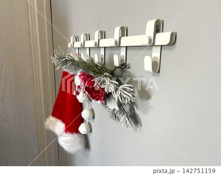 A red Santa hat with white trim hangs on a row of white hooks. A red Santa hat with white trim hangs on a row of white hooks. 142751159