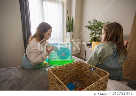 young girl and an adult are in a bedroom preparing a hamster cage. They are talking young girl and an adult are in a bedroom preparing a hamster cage. They are talking 142751473