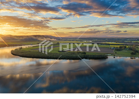 Aerial view over the Clarence River and surrounding farmland at sunset near Yamba, with smoke from a fire drifting across the distant rural landscape beneath a colourful evening sky Aerial view over the Clarence River and surrounding farmland at sunset near Yamba, with smoke from a fire drifting across the distant rural landscape beneath a colourful evening sky 142752394