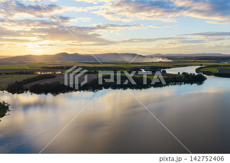 Aerial view over the Clarence River and surrounding farmland at sunset near Yamba, with smoke from a fire drifting across the distant rural landscape beneath a colourful evening sky  142752406