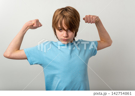 Young preteen boy in a light blue tee flexing biceps and staring confidently at the camera, conveying strength, determination and self esteem on a clean white background Young preteen boy in a light blue tee flexing biceps and staring confidently at the camera, conveying strength, determination and self esteem on a clean white background 142754861