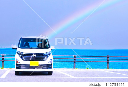 海辺の駐車場にとめた白い軽自動車と鮮やかなレインボー 142755423