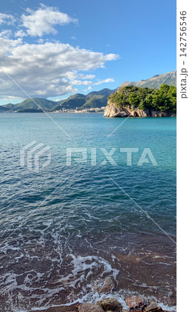 Turquoise mediterranean sea bay viewed from rocky beach under bright afternoon sun with mountain ranges stretching across the horizon amidst soft white clouds Turquoise mediterranean sea bay viewed from rocky beach under bright afternoon sun with mountain ranges stretching across the horizon amidst soft white clouds 142756546