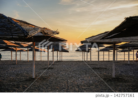 Rows of Straw Beach Umbrellas on Empty Beach at Sunset Rows of Straw Beach Umbrellas on Empty Beach at Sunset 142757161