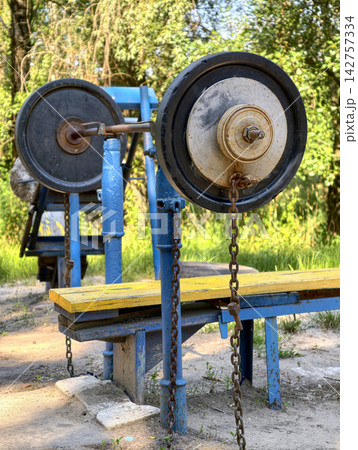 Loaded barbell with rubber and iron weight plates placed on a yellow horizontal bench at a shared outdoor gym area for chest training and muscle development 142757334