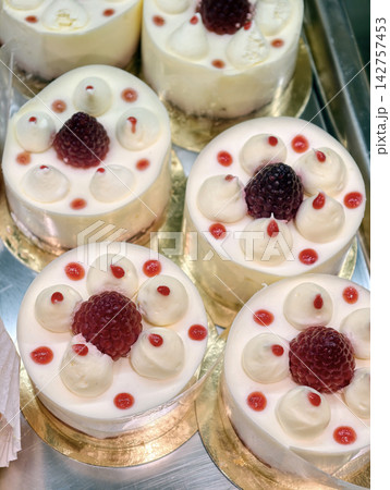 White pastries feature a cream decoration and one real raspberry placed in the center, creating a refined and visually appealing sweet dessert presentation 142757453