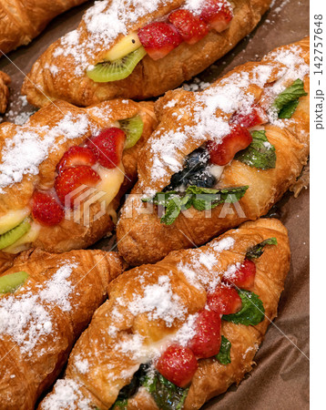 Fresh croissants with strawberry kiwi and blueberry filling displayed in a bakery, showcasing sweet pastries dusted with powdered sugar and arranged for customers Fresh croissants with strawberry kiwi and blueberry filling displayed in a bakery, showcasing sweet pastries dusted with powdered sugar and arranged for customers 142757648