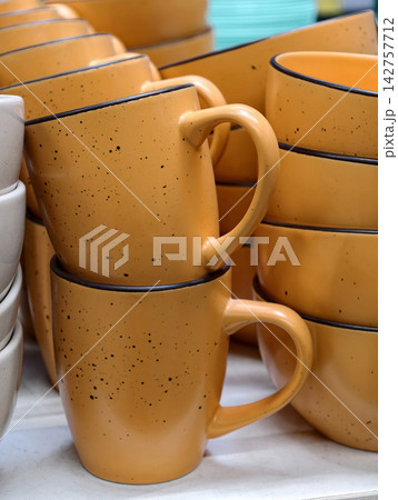 Ceramic orange cups paired with orange plates arranged on retail store shelving showing a basic tableware assortment intended for daily kitchen use and hypermarket presentation 142757712