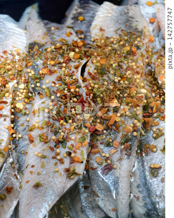 Herring fillet in seasoned oil displayed on a supermarket seafood counter, presenting prepared fish with spices in the refrigerated fish department 142757747