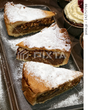 Three pieces of nut pie sprinkled with powdered sugar displayed in a bakery, showcasing fresh sweet pastries arranged attractively for customers on the counter Three pieces of nut pie sprinkled with powdered sugar displayed in a bakery, showcasing fresh sweet pastries arranged attractively for customers on the counter 142757788