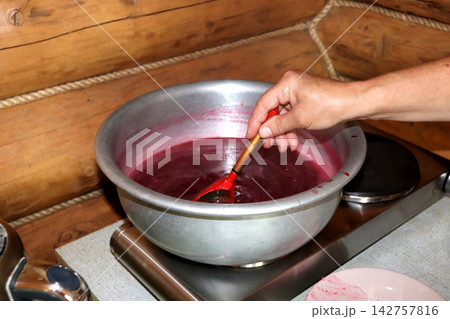 A woman cooks redcurrant jelly in a metal basin on an electric hot plate A woman cooks redcurrant jelly in a metal basin on an electric hot plate 142757816