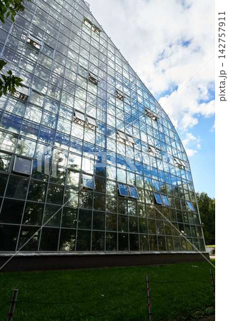 Facade of glass office building with grid of panes and metal frames reflecting blue sky and clouds from angled perspective showcasing modern architecture and glassy exterior Facade of glass office building with grid of panes and metal frames reflecting blue sky and clouds from angled perspective showcasing modern architecture and glassy exterior 142757911