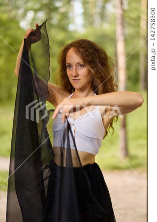 Redhaired woman gazes thoughtfully while holding delicate chiffon fabric 142758300