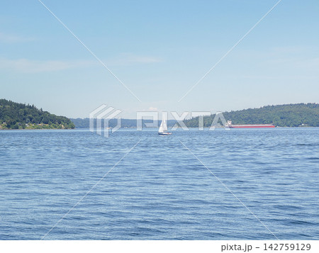 Distant sailboat and a cargo ship on Puget Sound under a bright sky in Ruston, WA. Distant sailboat and a cargo ship on Puget Sound under a bright sky in Ruston, WA. 142759129