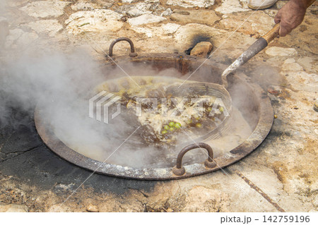Submerging wire basket of white grapes in boiling cauldron during traditional escalda process for sun drying Submerging wire basket of white grapes in boiling cauldron during traditional escalda process for sun drying 142759196