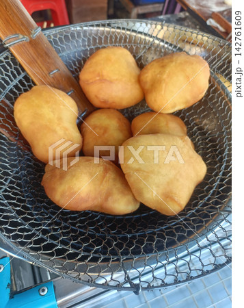 Golden fried dough fritter in wire basket at outdoor food stall 142761609