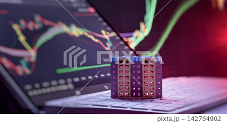Digital property trading and mortgage rates. Toy apartment house on computer keyboard against blurred stock market graphs. 142764902