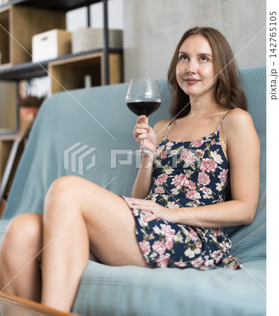Brunette woman relaxing on sofa with a glass of red wine in living room Brunette woman relaxing on sofa with a glass of red wine in living room 142765105