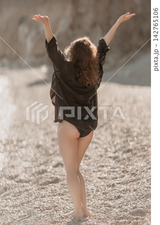 Woman beach freedom standing with arms raised on a rocky shore enjoying a sunny day of summer vacation lifestyle 142765106