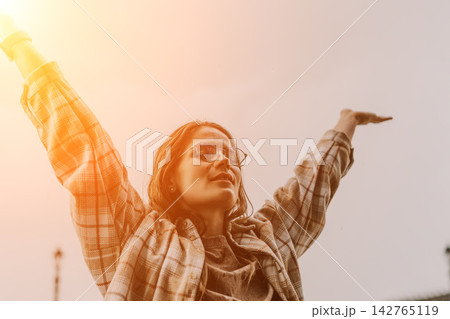 Woman freedom joy stands with arms raised high against the sky at sunset feeling happy and successful Woman freedom joy stands with arms raised high against the sky at sunset feeling happy and successful 142765119