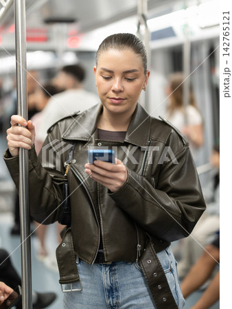 Girl stands in subway car and writes message on her smartphone screen Girl stands in subway car and writes message on her smartphone screen 142765121