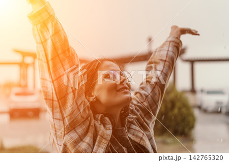 Woman rain happiness smiling young female raising arms outdoors during a golden hour summer shower enjoying freedom and joy 142765320