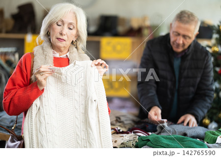 Uncertain mature woman choosing sweater in clothing store Uncertain mature woman choosing sweater in clothing store 142765590
