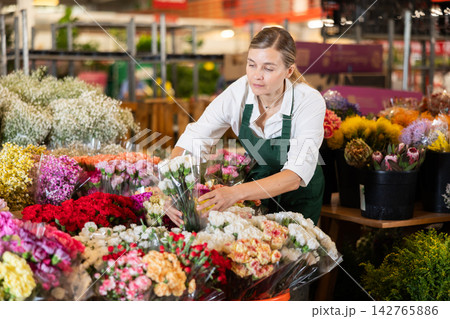 Woman flower shop assistant collects carnations into bouquet 142765886
