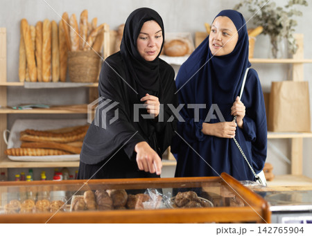 Two Muslim women pick up pastry in bakery Two Muslim women pick up pastry in bakery 142765904