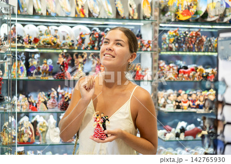 Female tourist happily chooses various souvenir figurines in spanish souvenir shop Female tourist happily chooses various souvenir figurines in spanish souvenir shop 142765930