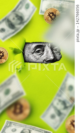 Dollar bills and coins are scattered around a green background with a close-up of a bill peeking through a torn paper hole 142766056