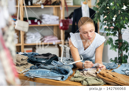 Young girl chooses fashionable jeans or shorts in clothing store for summer season Young girl chooses fashionable jeans or shorts in clothing store for summer season 142766068