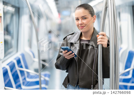 Young woman stands in subway car with phone 142766098