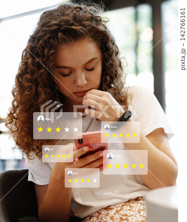 User reads reviews on a smartphone while sitting in a cafe with natural light coming in 142766161