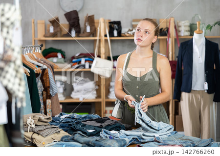 Woman standing in the store and choosing pants and shorts Woman standing in the store and choosing pants and shorts 142766260