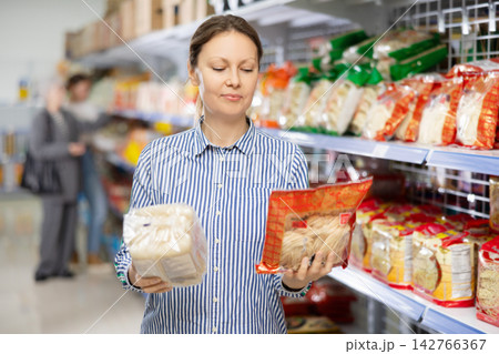 Interested woman reading label on packages of Asian noodles in supermarket Interested woman reading label on packages of Asian noodles in supermarket 142766367