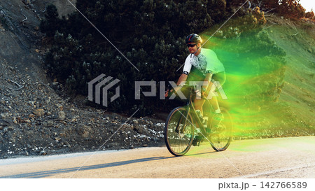 Cyclist riding along a road with greenery and hills in the background during daylight hours Cyclist riding along a road with greenery and hills in the background during daylight hours 142766589