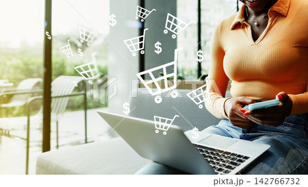 Engaging in online shopping while sitting on a couch with a laptop and phone in hand Engaging in online shopping while sitting on a couch with a laptop and phone in hand 142766732